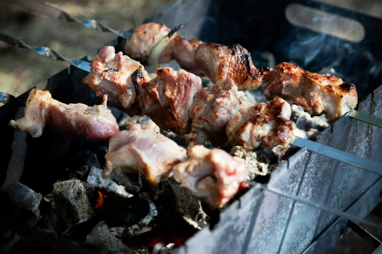 Espetos de carne sobre uma churrasqueira a carvão, com fumaça ao fundo
